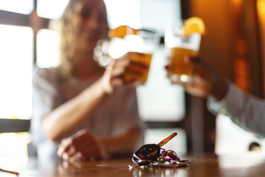 A man and and woman drinking cocktails in a bar with car keys visible.